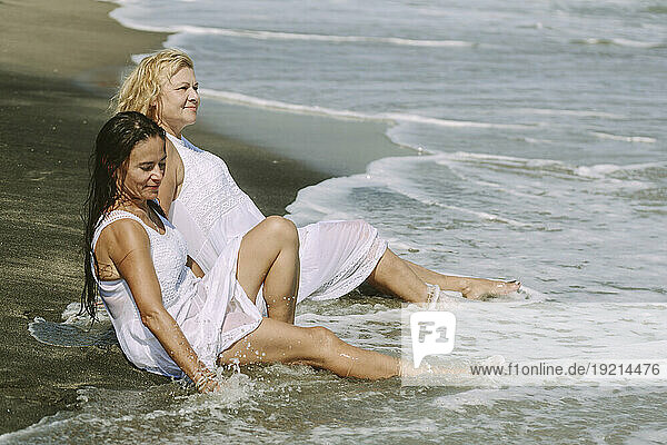 Senior woman sitting with friend on shore at beach
