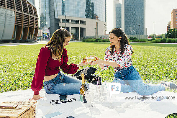 Happy woman giving gift to friend and enjoying picnic in park
