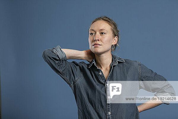Contemplative woman with hand behind head against blue background