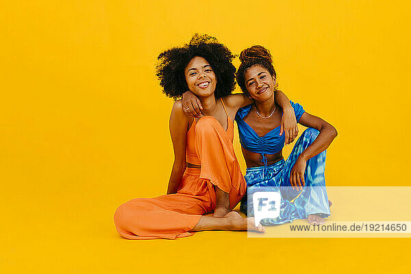 Happy friends with arm around sitting against yellow background
