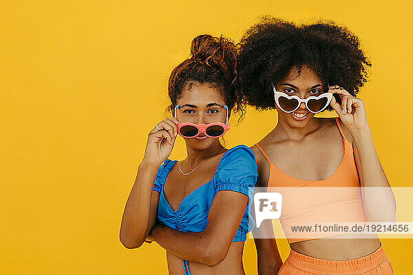 Multiracial friends wearing sunglasses against yellow background
