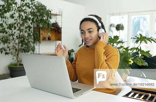 Freelancer doing video call over laptop using wireless headphones at home office