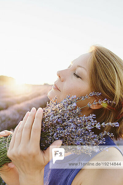 Serene woman holding bunch of lavender flowers in field