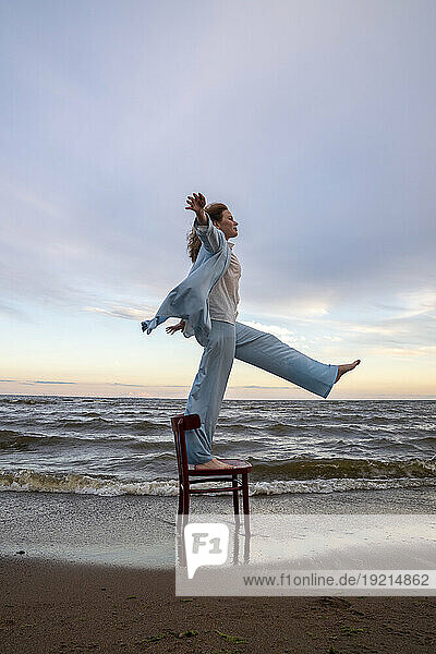 Woman standing and balancing on chair at beach