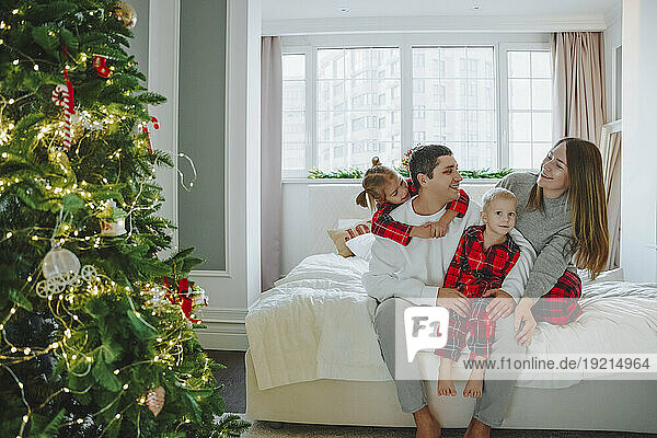 Family sitting on bed near Christmas tree at home