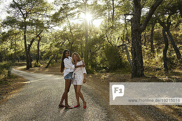 Teenage girl hugging mother standing on road in forest at sunset
