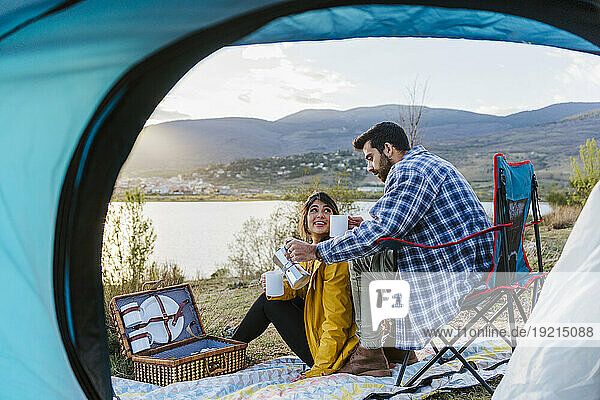Boyfriend serving coffee to girlfriend sitting near tent