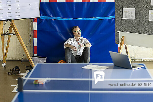 Thoughtful businessman sitting behind tennis table in office