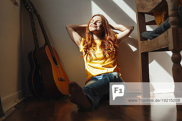 Smiling redhead woman with hands behind head sitting on floor