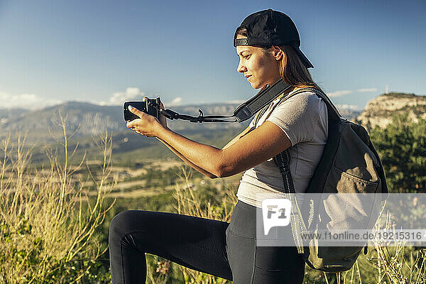 Young woman with backpack photographing on sunny day