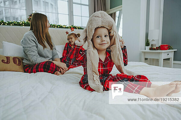 Boy wearing animal hat sitting on bed with family at home