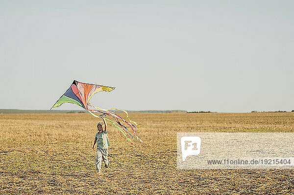 Cheerful boy flying kite and running in meadow