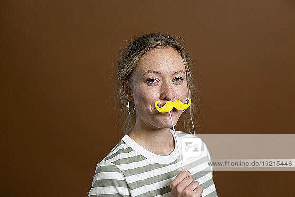Blond woman holding mustache prop in studio