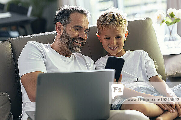 Smiling Father sharing smart phone with son in living room