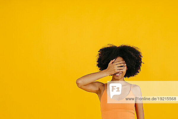 Smiling woman covering eyes against yellow background