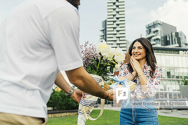 Man giving gift box and bouquet of flowers to happy woman