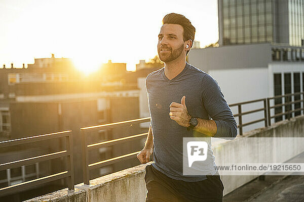 Active man running by railing on terrace at sunset