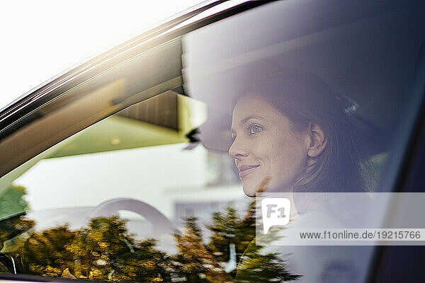 Smiling woman driving electric car seen through window