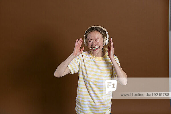 Woman laughing and listening music through headphones over brown background