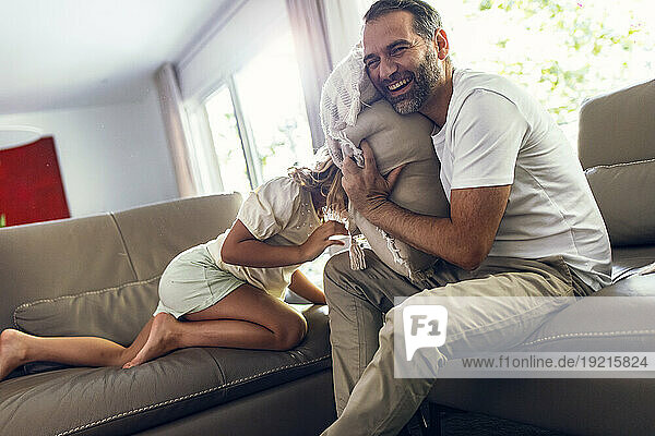 Happy father enjoys playing with daughter on sofa