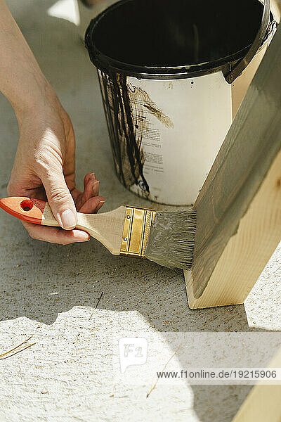 Hand of worker painting plank with paintbrush on sunny day