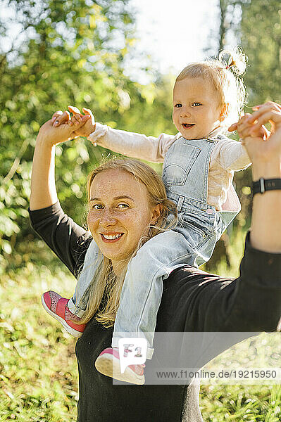 Smiling mother carrying daughter on shoulders in park