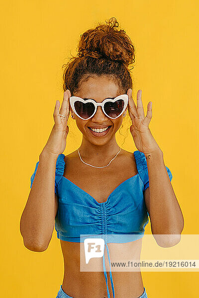 Smiling woman wearing heart shape sunglasses against yellow background