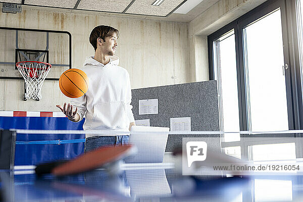 Young businessman playing with basketball in office