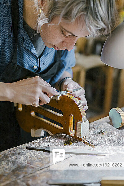 Craftsperson shaping violin with rasp in workshop
