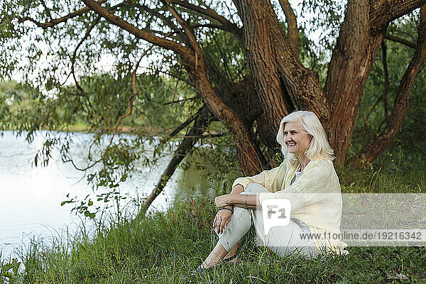 Happy mature woman sitting at lakeshore