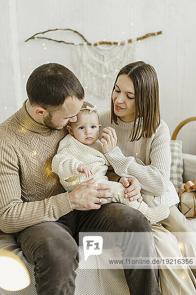 Smiling parents sitting with baby daughter on sofa at home