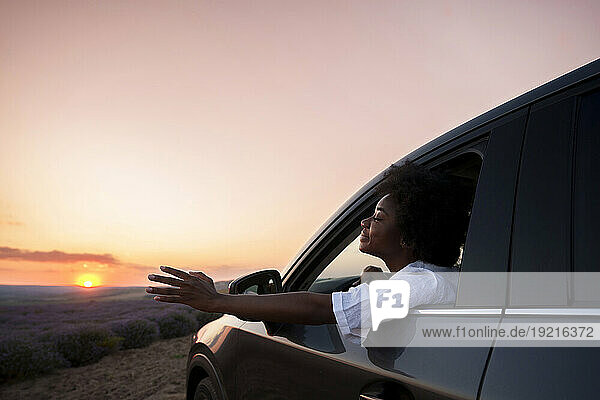 Woman with eyes closed leaning out of car window at sunset