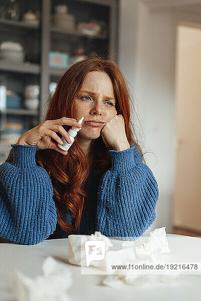 Sad sick woman sitting with medicine and tissue papers at table