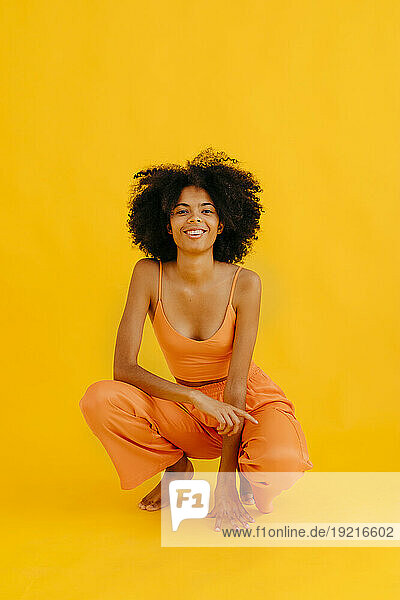 Smiling woman with curly hair crouching against yellow background