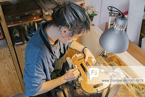 Luthier making parts of violin on desk in workshop