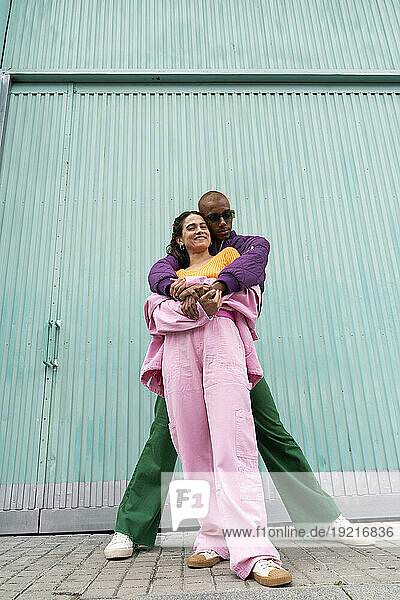 Happy fashionable couple standing together in front of blue shutter door