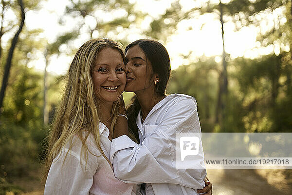 Teenage girl kissing happy mother in forest at sunset