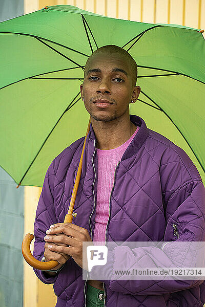 Non-binary person holding green umbrella