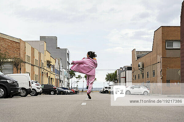 Cheerful woman jumping and walking on road under sky