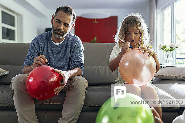 Daughter and father drawing on balloons sitting in living room