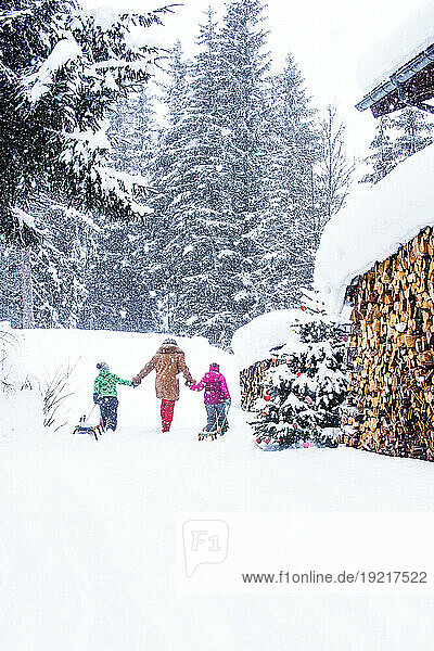 Grandmother holding hands and walking with children pulling sled on snow