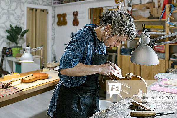 Luthier carving on violin at desk in workshop
