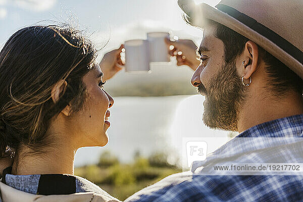 Couple toasting coffee mugs on sunny day