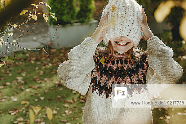 Smiling girl covering face with knit hat in garden