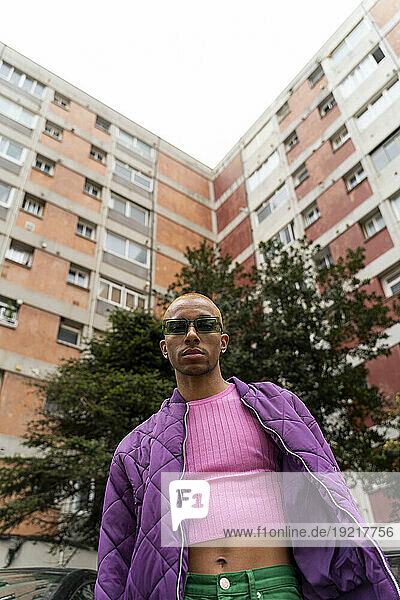 Non-binary person wearing sunglasses standing in front of building