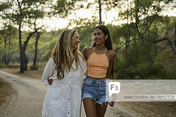 Smiling mother and daughter with arms around walking on road in forest