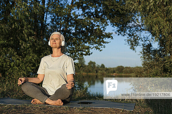 Mature woman listening to music sitting on exercise mat