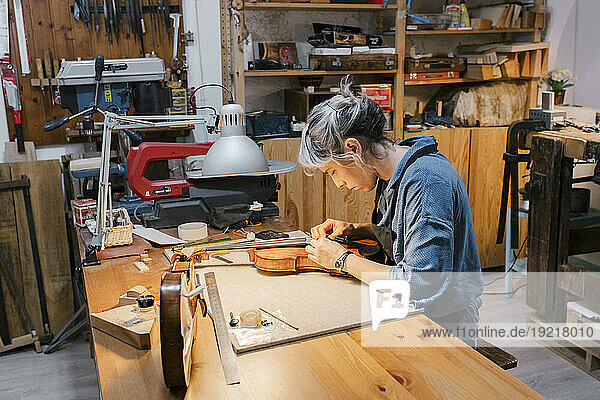 Female craftsperson working on violin at desk in workshop