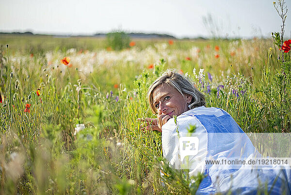 Smiling woman looking over shoulder lying down in meadow
