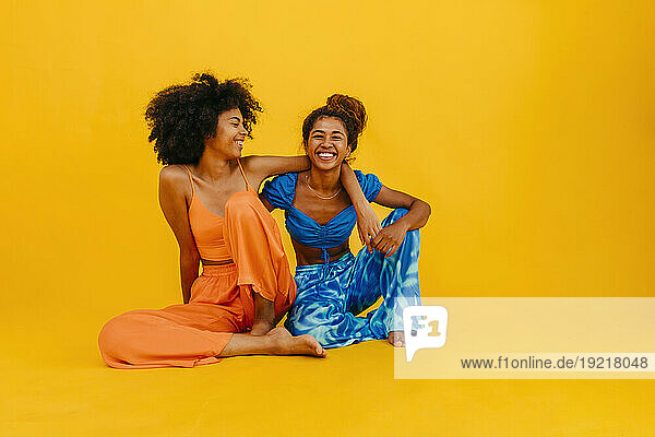 Happy young friends sitting against yellow background